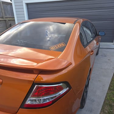 An orange sedan parked in a driveway in front of a gray garage door, viewed from the rear three-quarter angle.
